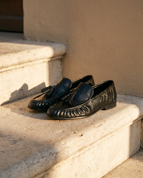 Paire de mocassins ADELINE noirs posée sur une marche en pierre — A by André