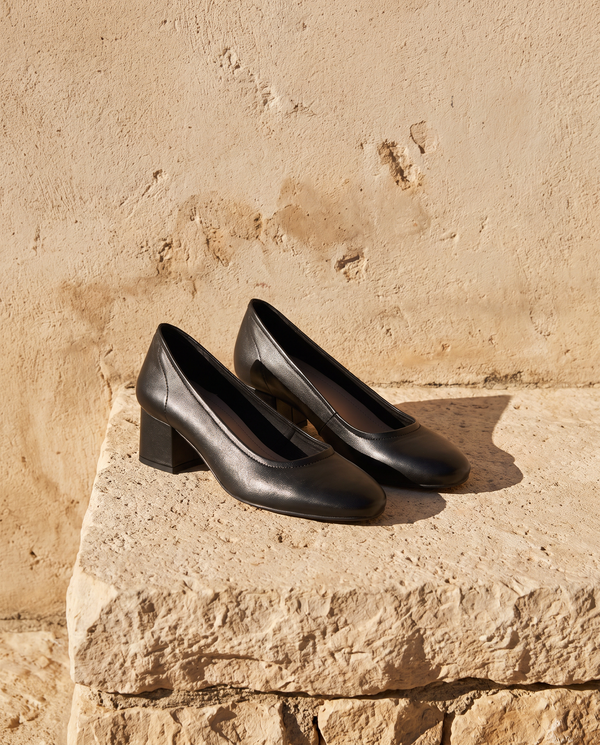 Escarpin NINAROSE noir posé sur une marche en pierre, mur enduit beige