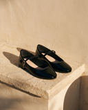 Ballerine AGATHE noire posée sur une marche en pierre, mur enduit beige