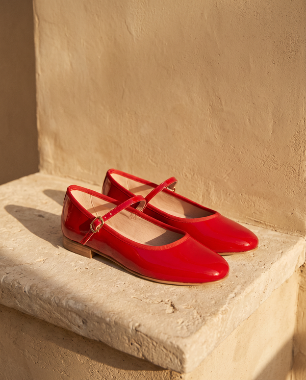 Ballerine AGATHE rouge posée sur une marche en pierre, mur enduit beige