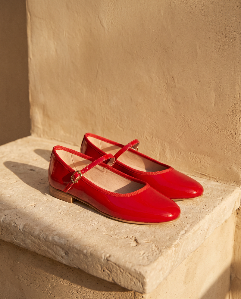 Ballerine AGATHE rouge posée sur une marche en pierre, mur enduit beige