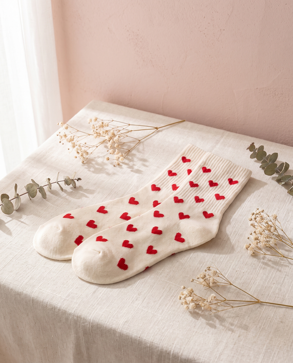 Chaussettes cœurs Aglae, posées sur un lin crème, mur rose poudré
