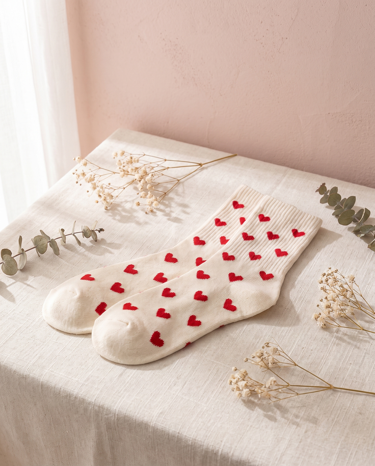Chaussettes cœurs Aglae, posées sur un lin crème, mur rose poudré