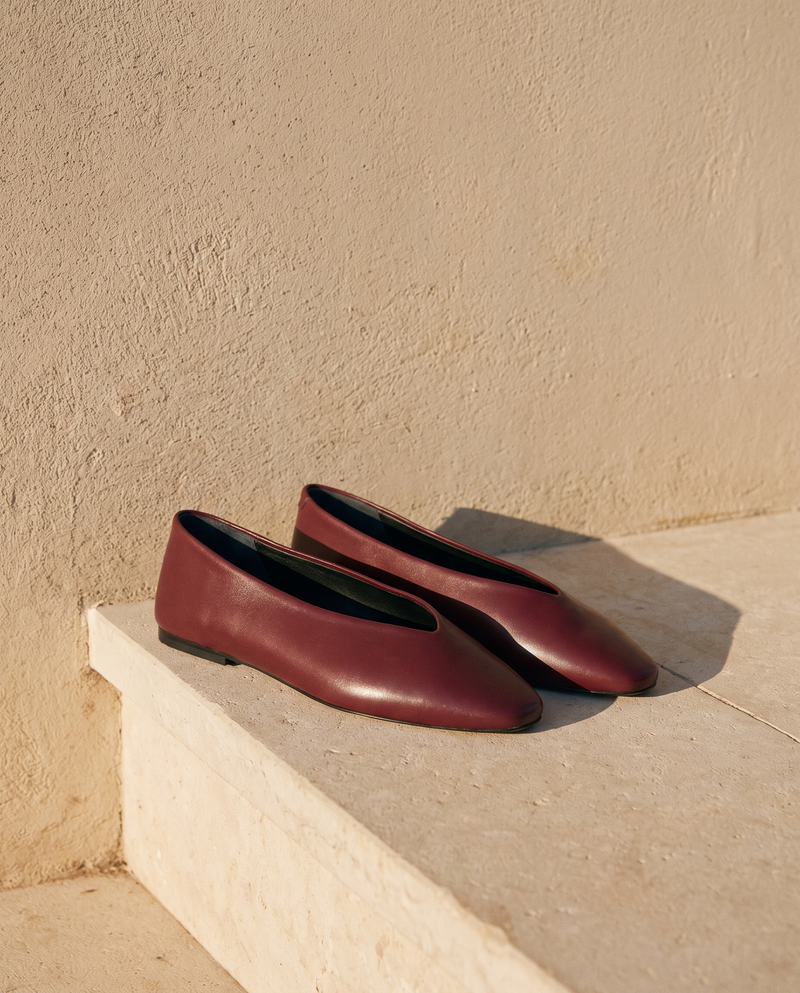 Ballerine AIRELLE bordeaux posée sur une marche en pierre, mur enduit beige