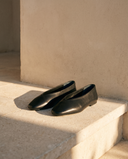 Ballerine AIRELLE noire posée sur une marche en pierre, mur enduit beige