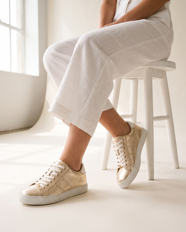 Basket BERKELEY dorée portée, gros plan, femme assise jambes croisées sur un tabouret blanc en studio