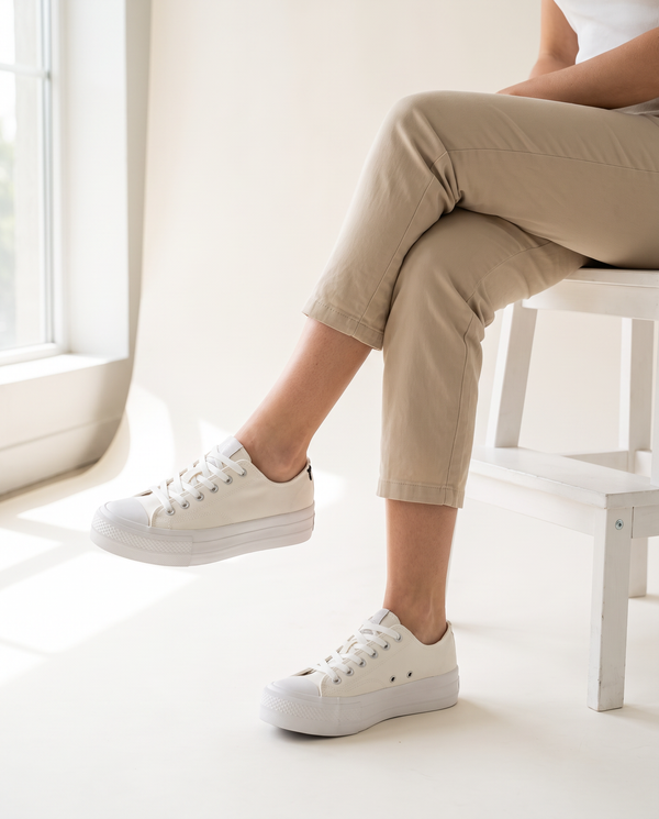 Basket CALAMA blanche portée, gros plan, femme assise jambes croisées sur un tabouret blanc en studio
