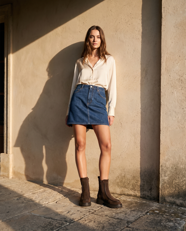 Boots CASSIE marron portées avec une jupe en jean sur une terrasse en pierre — A by André