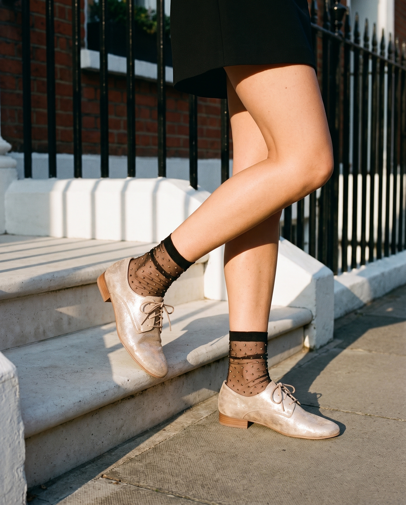 Derby COMPLICE doré porté, gros plan, un pied posé sur la marche d'une maison londonienne