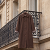Trench DALILA marron suspendu à une grille en fer, rue haussmannienne