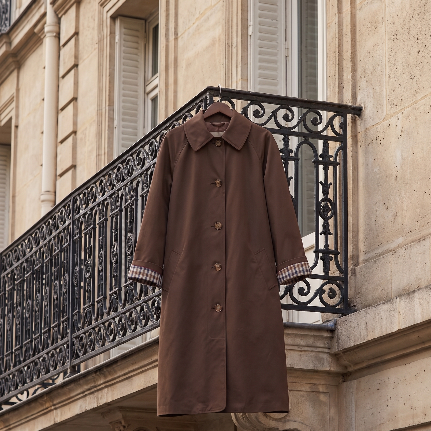 Trench DALILA marron suspendu à une grille en fer, rue haussmannienne
