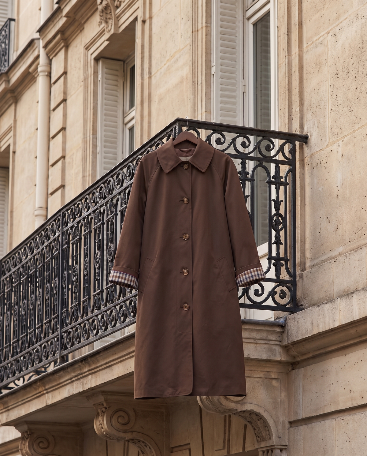 Trench DALILA marron suspendu à une grille en fer, rue haussmannienne