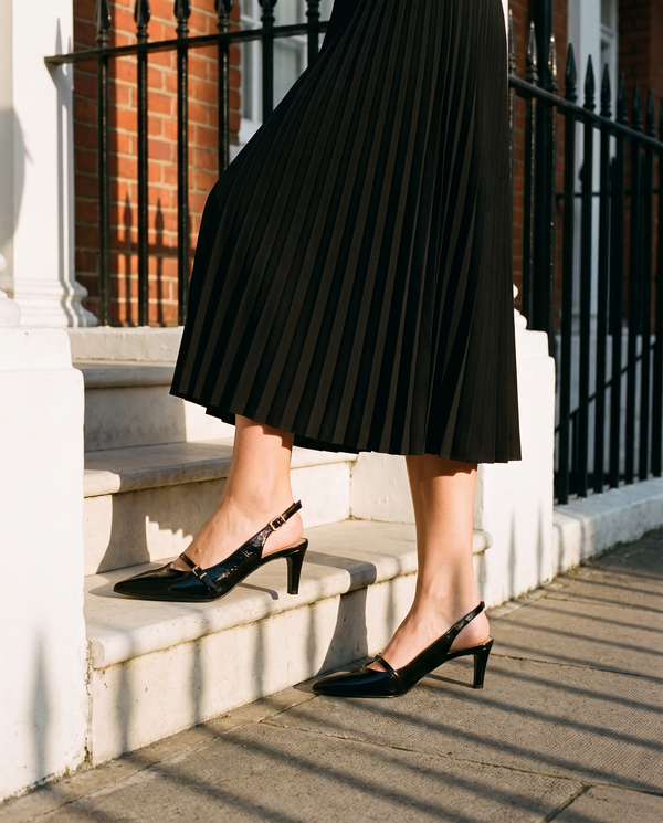 Slingback FIDJI noire portée, gros plan, un pied posé sur la marche d'une maison londonienne