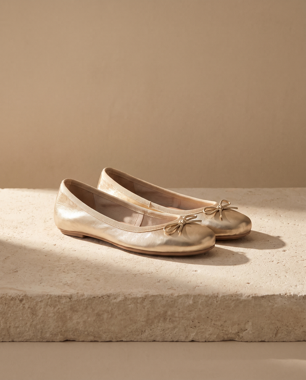 Ballerine GENIALE dorée posée sur une marche en pierre, mur enduit beige