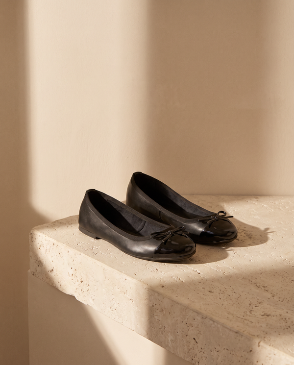 Ballerine GIULIA noire posée sur une marche en pierre, mur enduit beige
