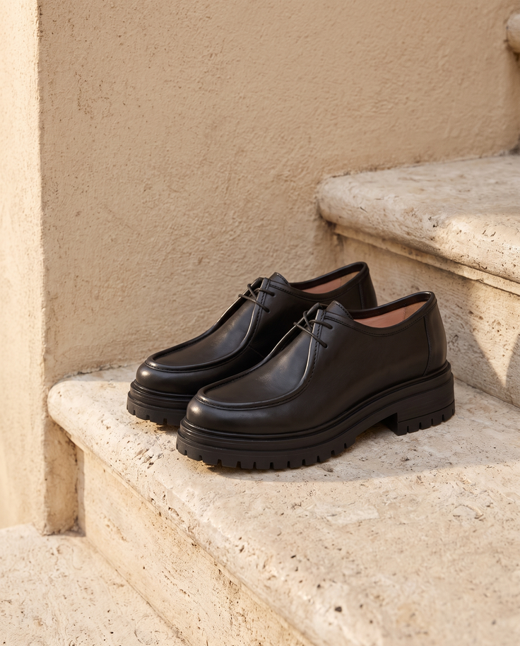 Derby GOMINETTE noir posé sur une marche en pierre, mur enduit beige
