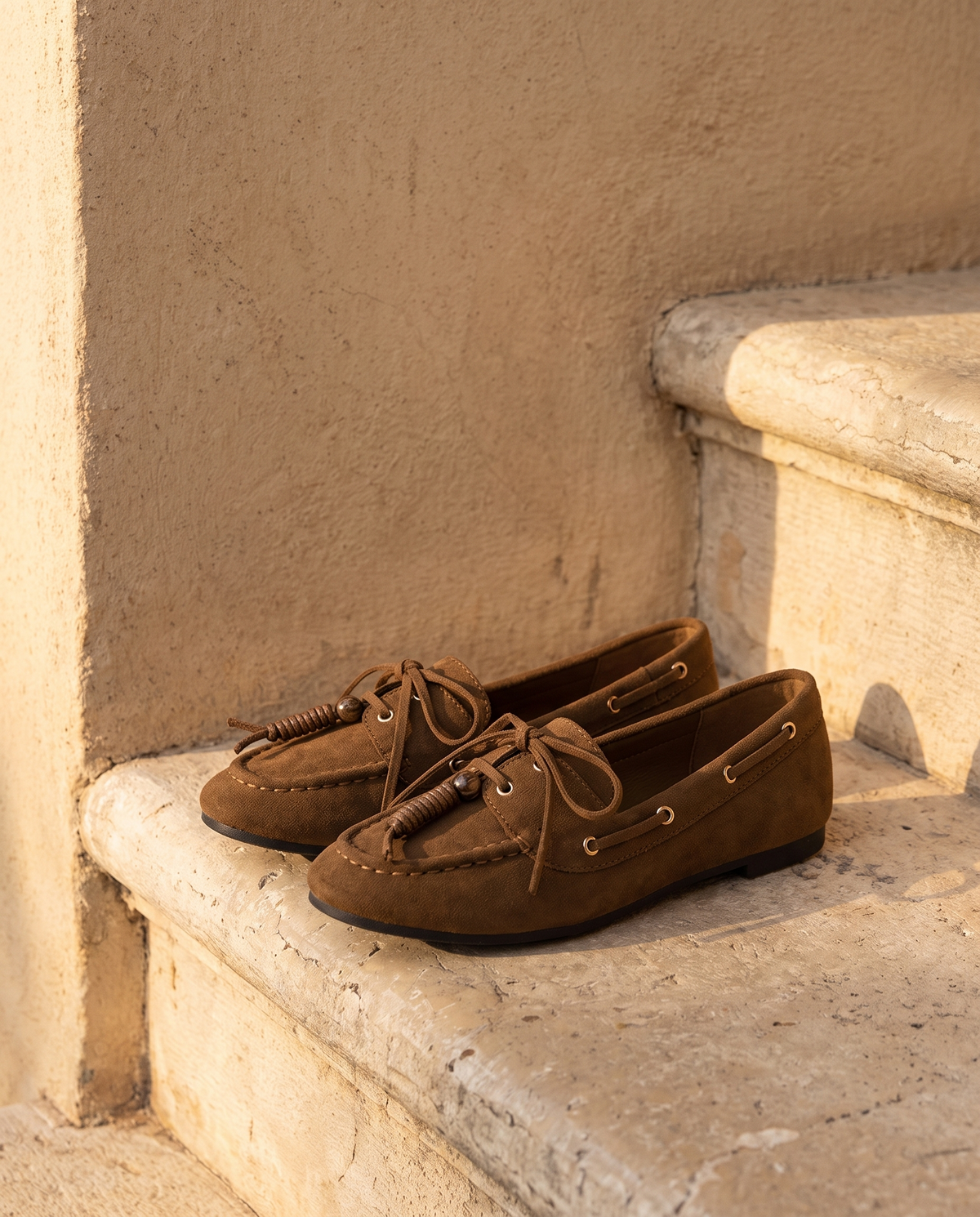 Derby ILONA camel posée sur une marche en pierre, mur enduit beige
