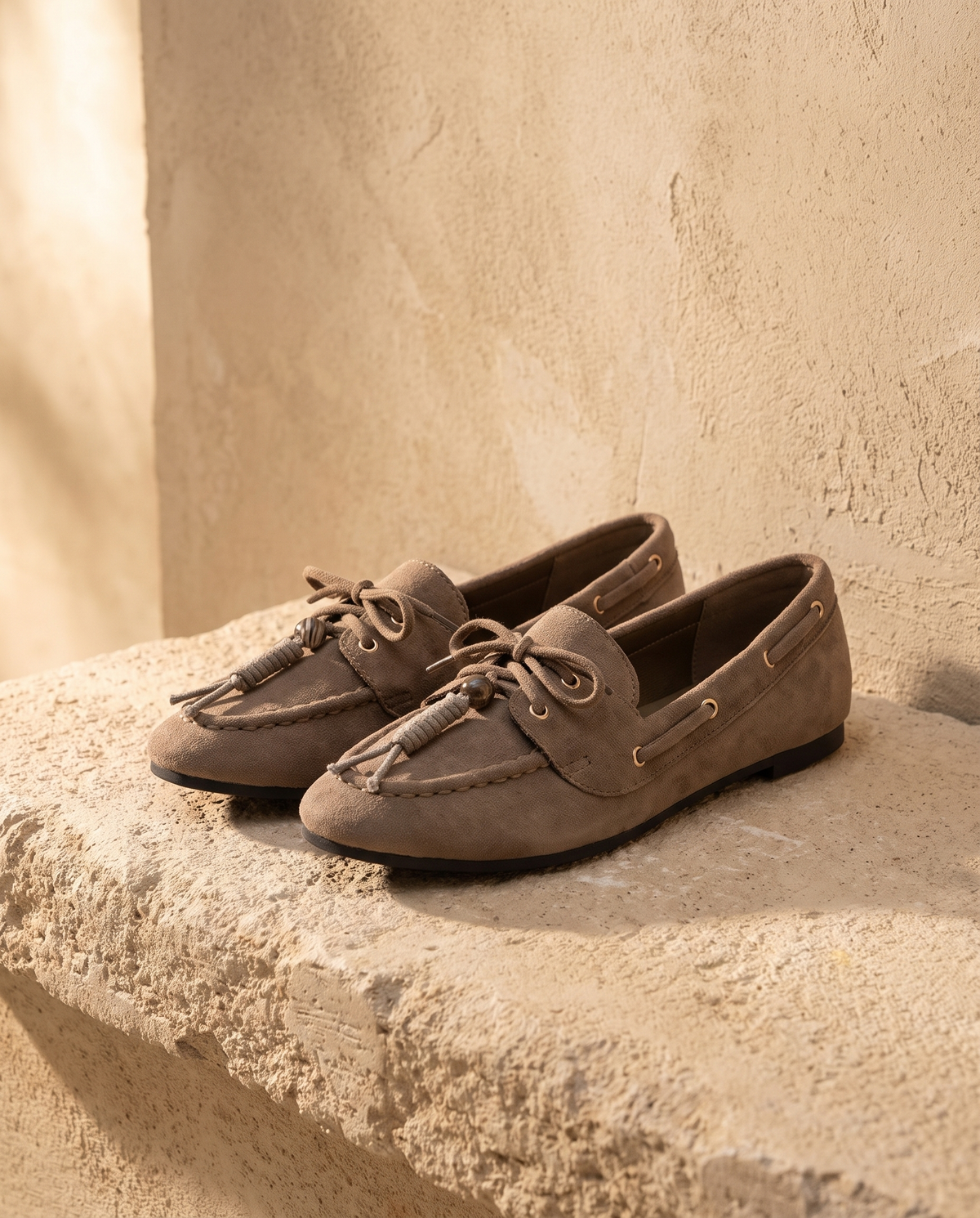 Derby ILONA taupe posée sur une marche en pierre, mur enduit beige