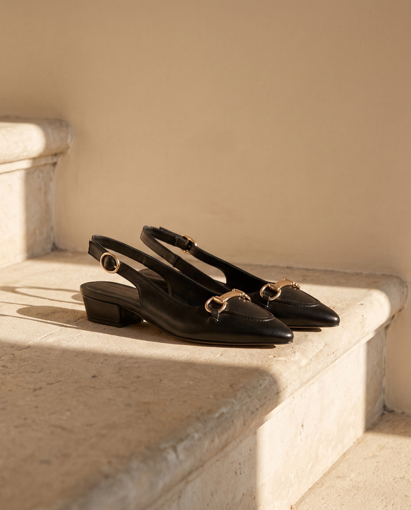Ballerine IOLANA noire posée sur une marche en pierre, mur enduit beige