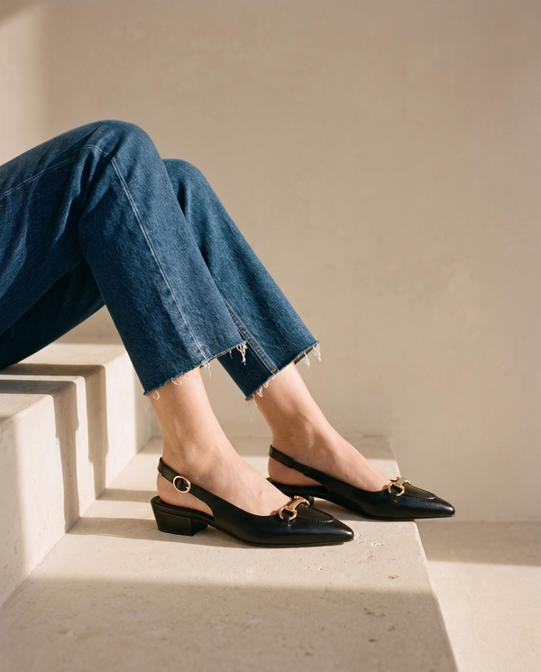 Ballerine IOLANA noire portée, assise sur une marche en pierre
