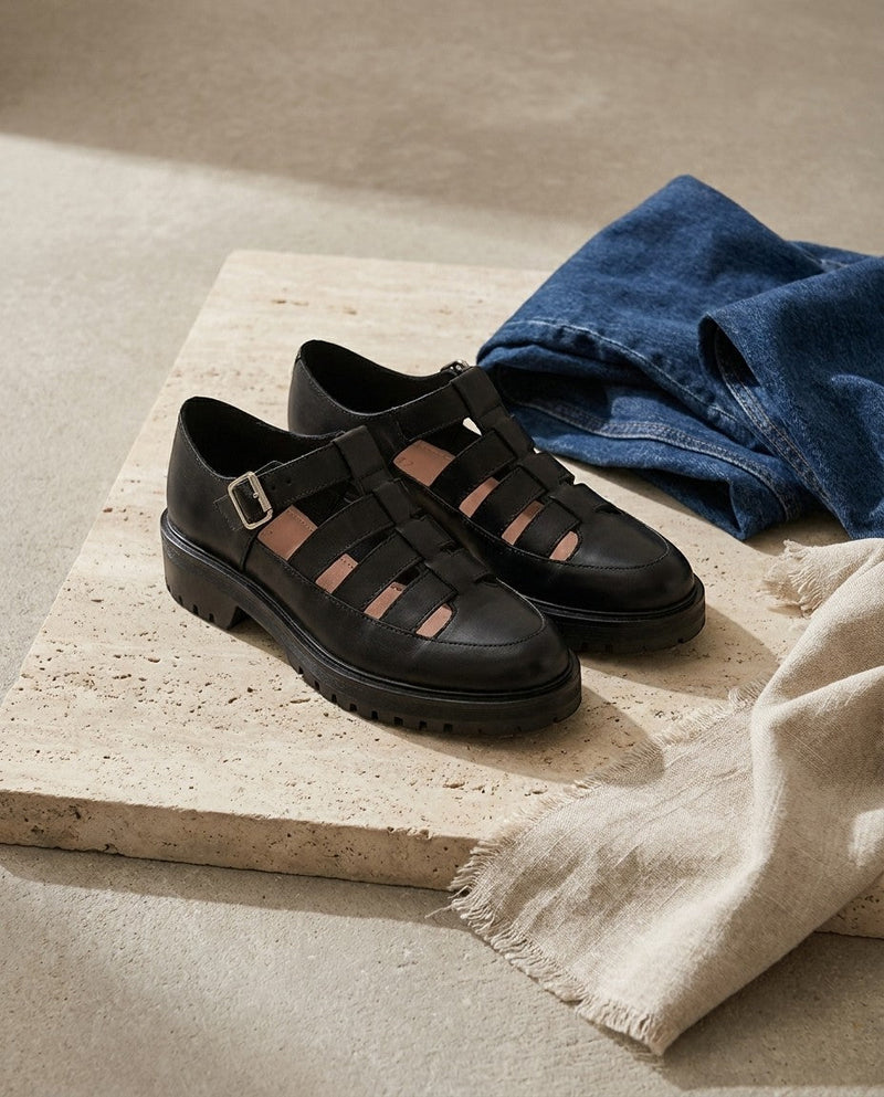 Derbies André Izzie en cuir noir avec brides ajourées et semelle crantée, posées sur une dalle en pierre