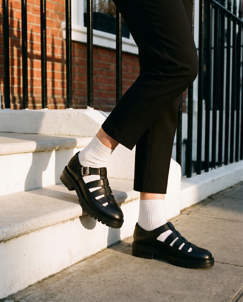 Derby IZZIE noir porté, gros plan, un pied posé sur la marche d'une maison londonienne