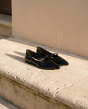 Ballerine JULIETTA noire posée sur une marche en pierre, mur enduit beige