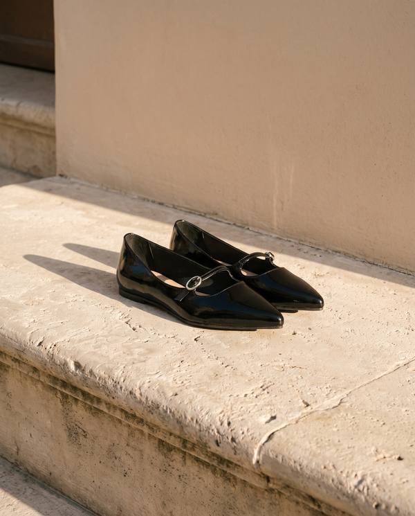 Ballerine JULIETTA noire posée sur une marche en pierre, mur enduit beige
