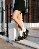 Derby KEICY noir porté, gros plan, un pied posé sur la marche d'une maison londonienne