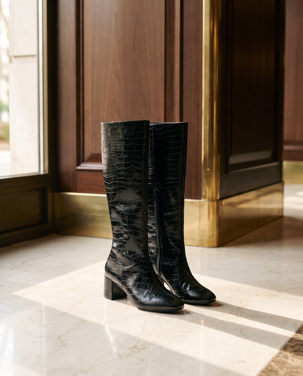 Paire de bottes LEZIA noires imprimé croco posée sur un sol en marbre d'hôtel — Maison André