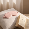 Masque de nuit en soie Ysia rose vichy posé sur un oreiller en lin, livre ouvert