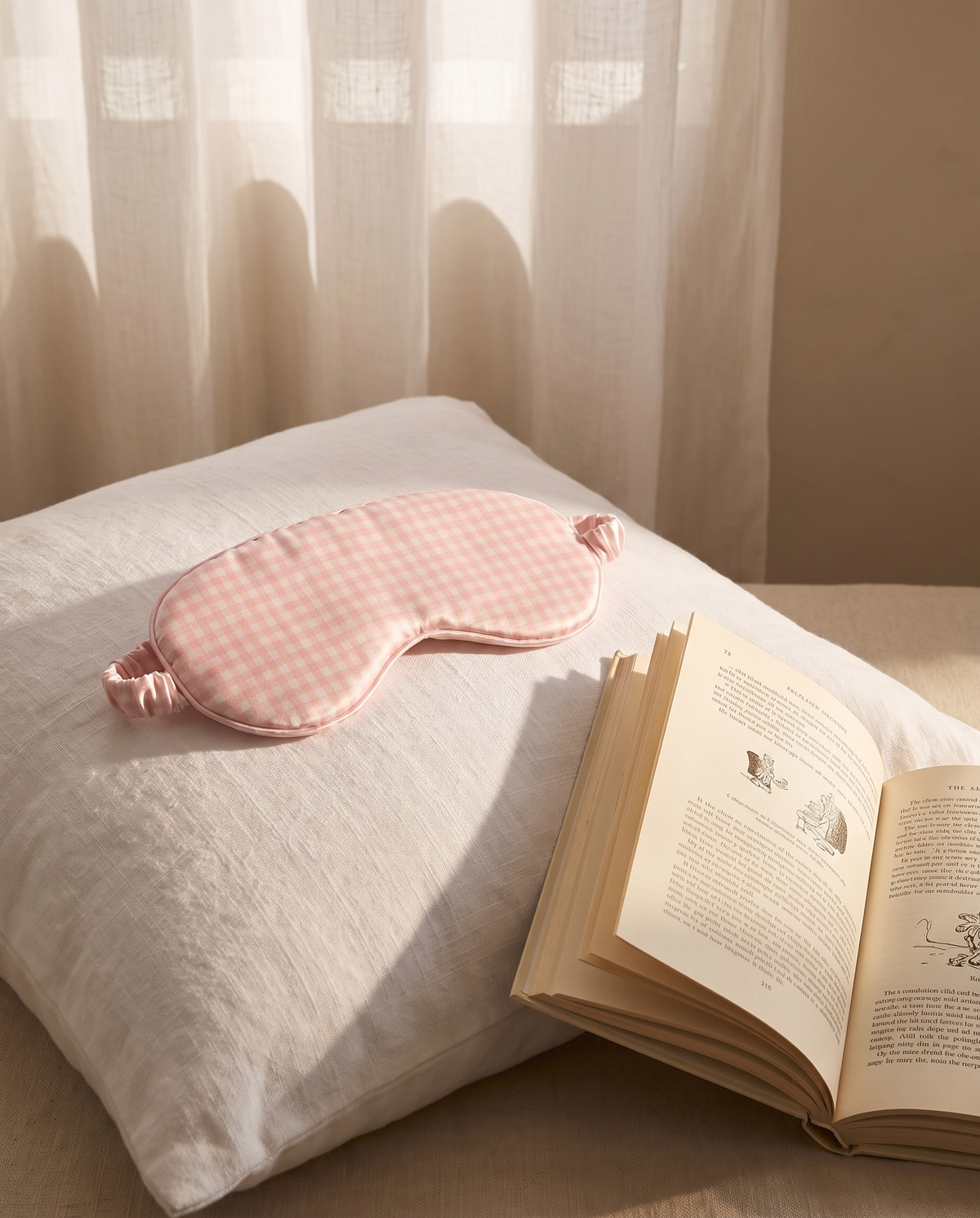 Masque de nuit en soie Ysia rose vichy posé sur un oreiller en lin, livre ouvert