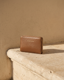 Petit portefeuille MINI BUCI bronze Maison André sur une marche en pierre