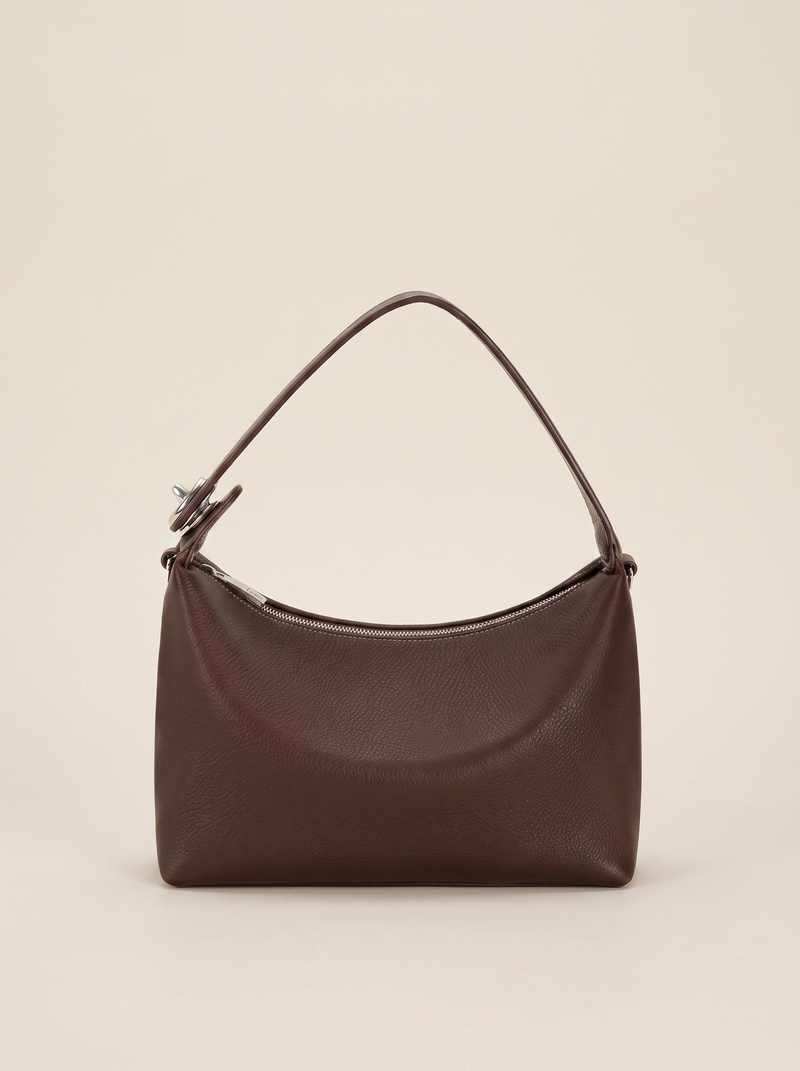 Sac demi-lune Miralie marron posé sur une marche en pierre de travertin, fond ivoire