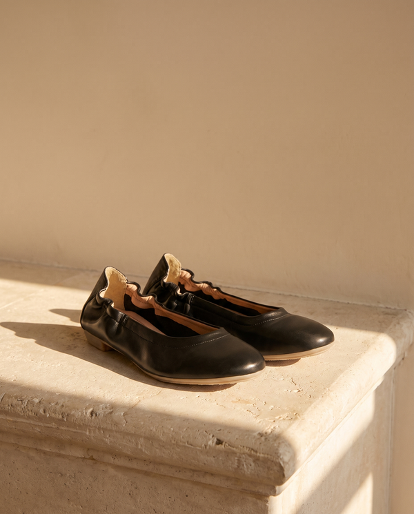Ballerine NINA noire posée sur une marche en pierre, mur enduit beige