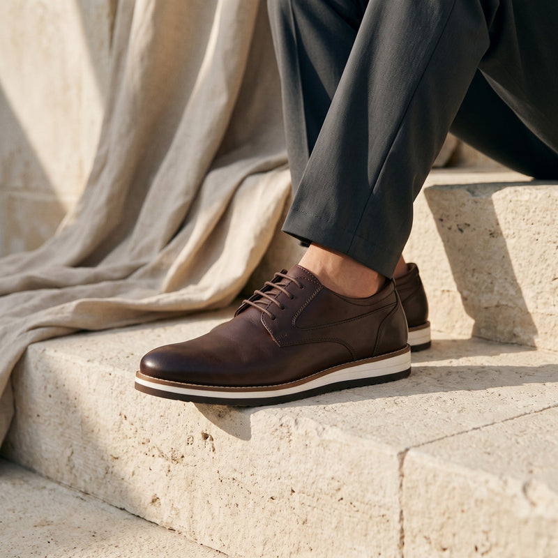 Chaussures de ville André Norwich marron en cuir avec semelle contrastante, portées sur des marches en pierre.