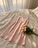 Nuisette courte en soie Selèna rose clair posée à plat sur un lit en lin, bouquet de roses