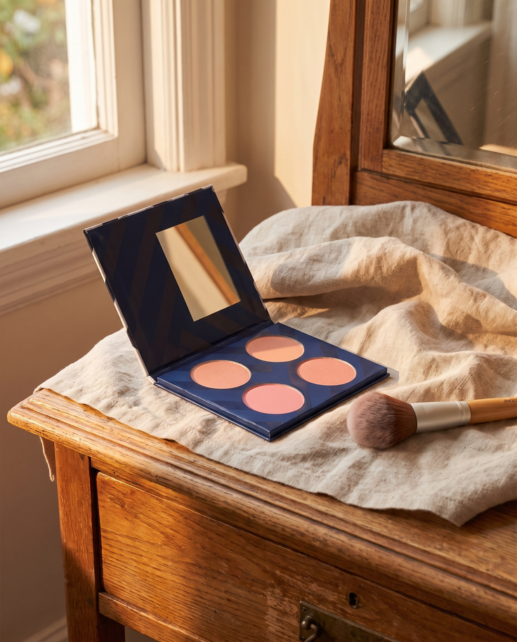 Palette de 4 blushs CXL by Christian Lacroix ouverte sur une coiffeuse en bois et lin, pinceau