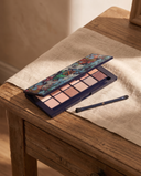 Palette fards à paupières Natural Nude CXL by Christian Lacroix ouverte sur une coiffeuse en bois et lin