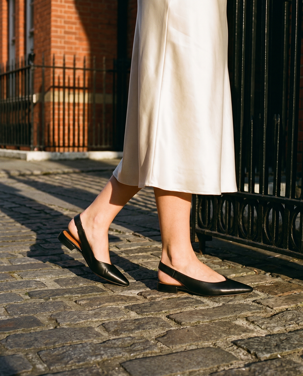 Slingback ROSEE noire portée, gros plan, sur les pavés d'une rue londonienne