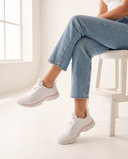 Basket SERAPIS blanche portée, gros plan, femme assise jambes croisées sur un tabouret blanc en studio