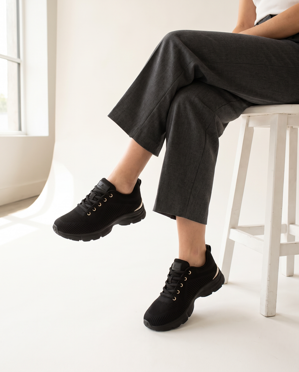 Basket SERAPIS noire portée, gros plan, femme assise jambes croisées sur un tabouret blanc en studio