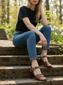 Sandales André Veloutine cognac en cuir avec talon bloc, portées par une femme assise sur des marches en pierre.